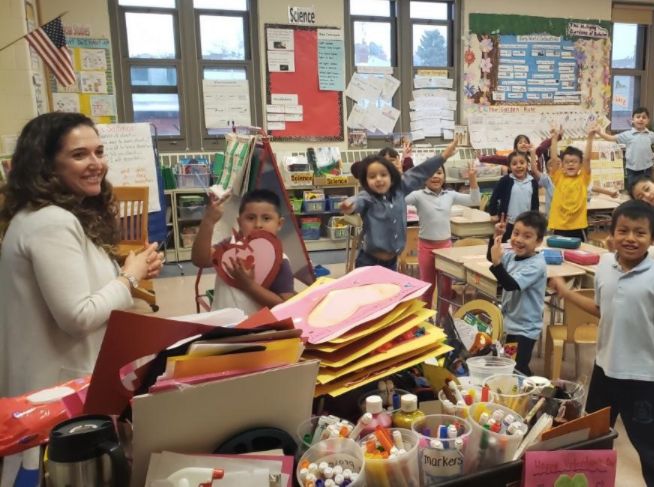 Students waving from their classroom beside a table of art supplies