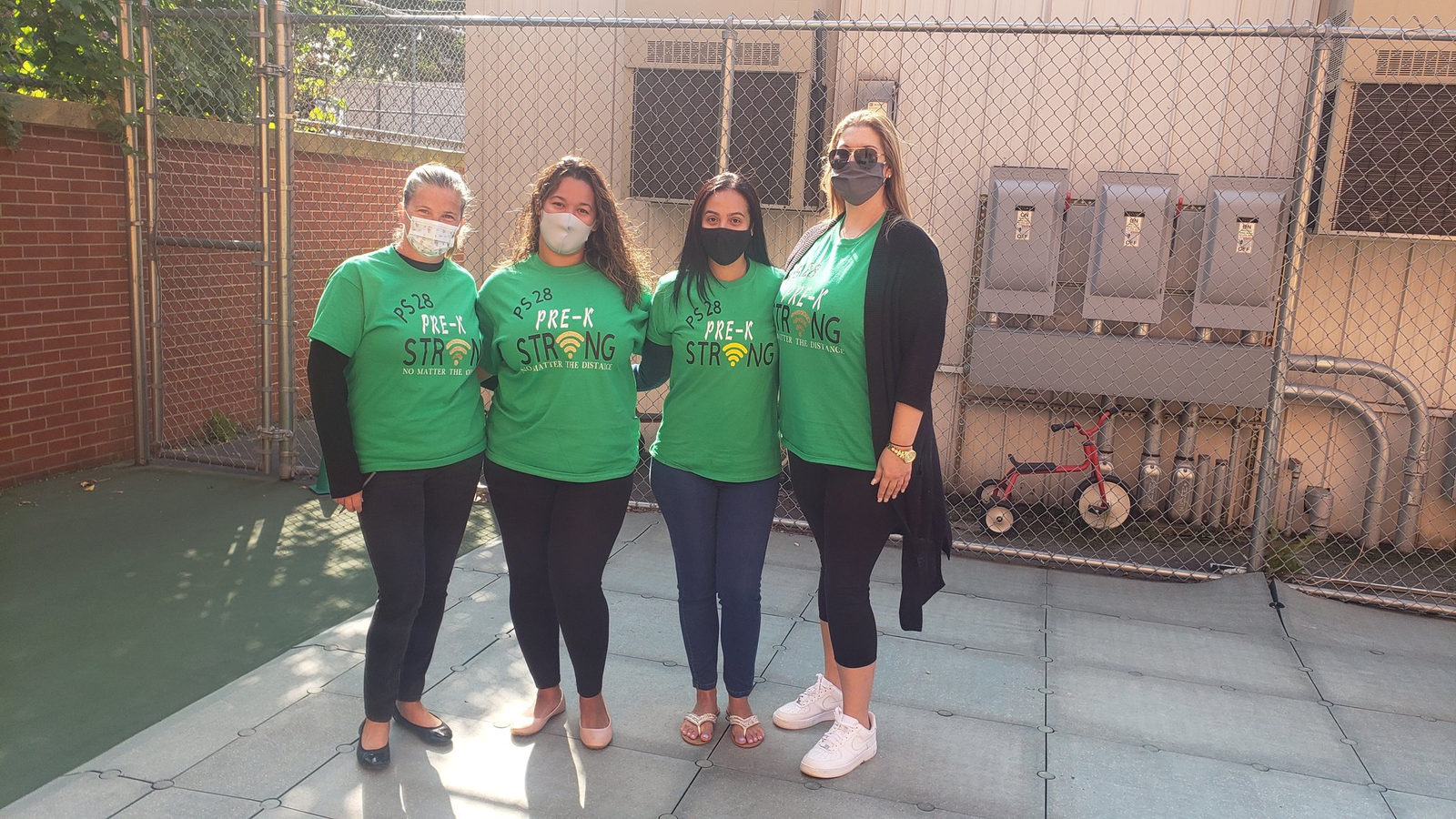 Four staff members in matching green shirts in the schoolyard