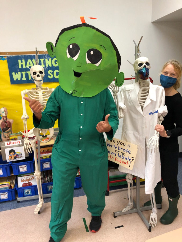 Z the green character in a science classroom with a skeleton and a teacher