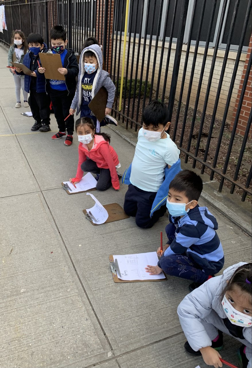Students kneeling on the sidewalk to write on their clipboards
