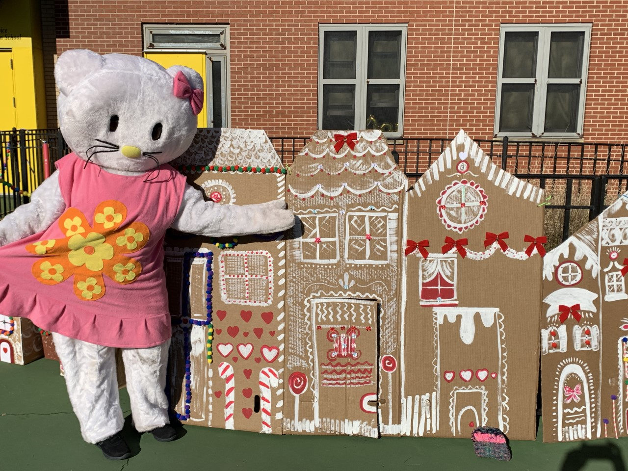 Costumed Hello Kitty character in front of cardboard gingerbread houses