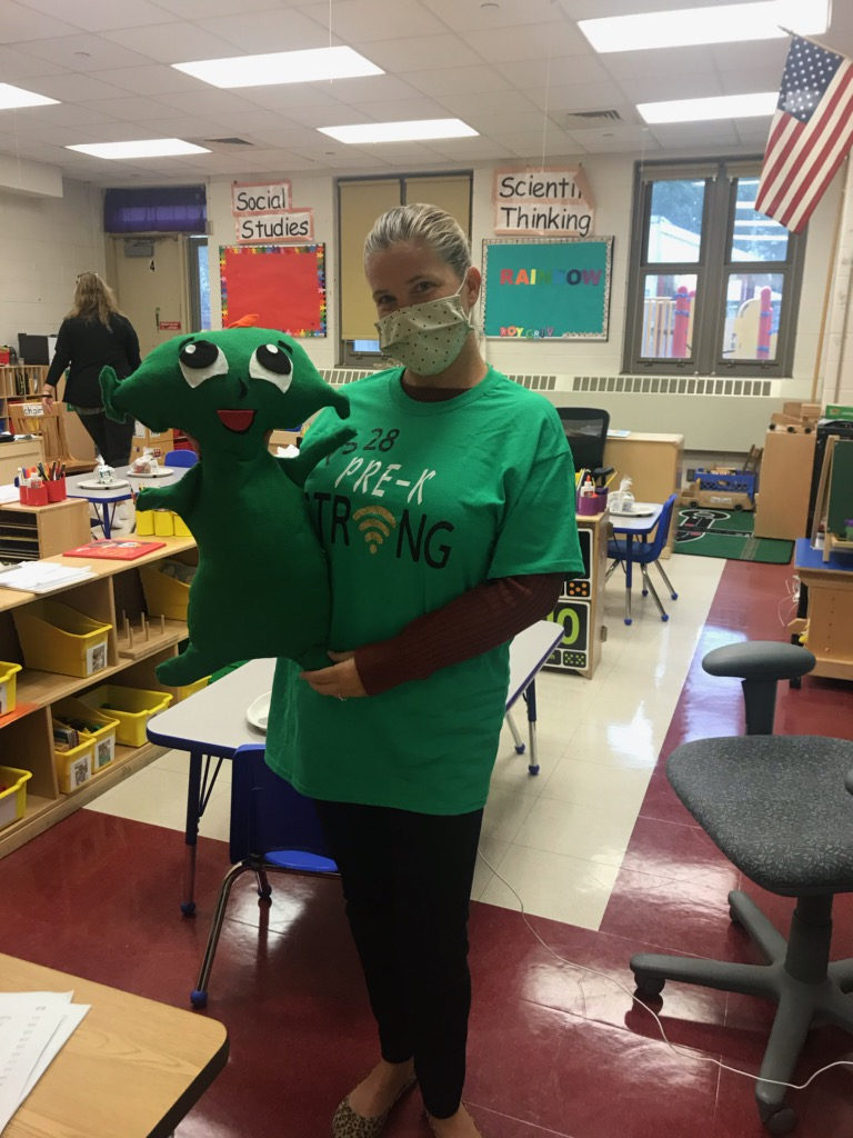 Teacher in a green shirt holding a green character doll in her classroom