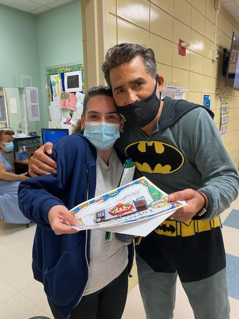 Principal in a Batman costume with a teacher holding a gift