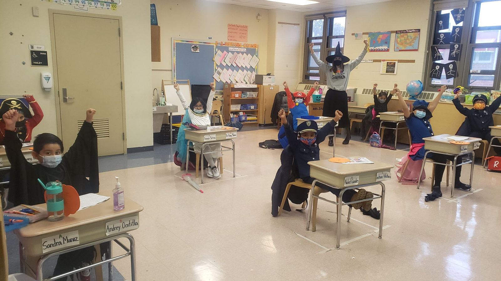 Students in costumes raising their hands at their desks