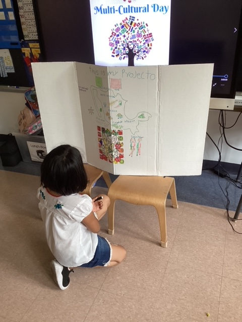 Student kneeling beside a trifold country project on Multicultural Day