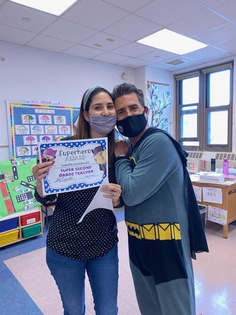 Principal in a Batman costume with a teacher holding a Superhero certificate