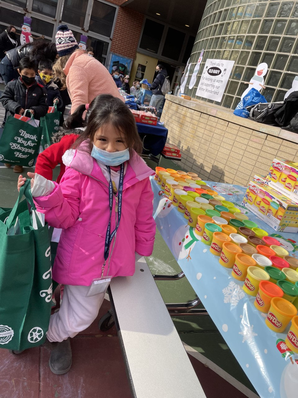 Student in a pink coat carrying a green gift bag past a table of gifts