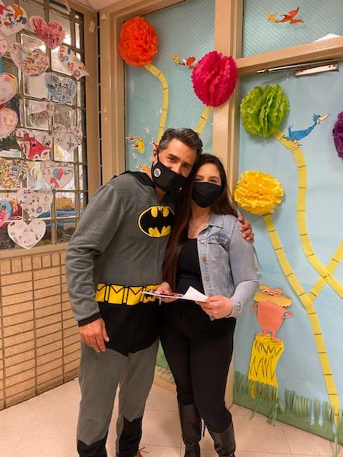 Principal in a Batman costume with a staff member by a decorated wall