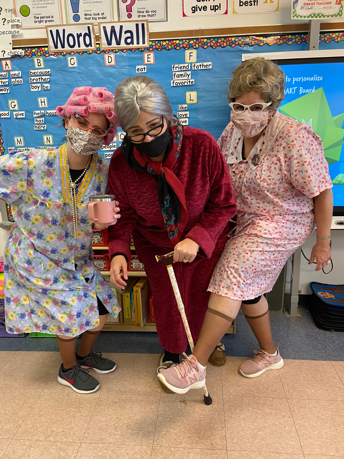 Three staff members dressed as grandparents in front of the word wall