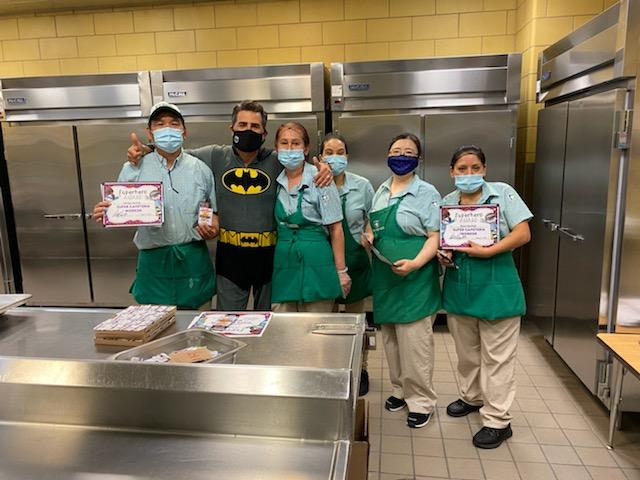 Principal in a Batman costume with the kitchen staff holding certificates
