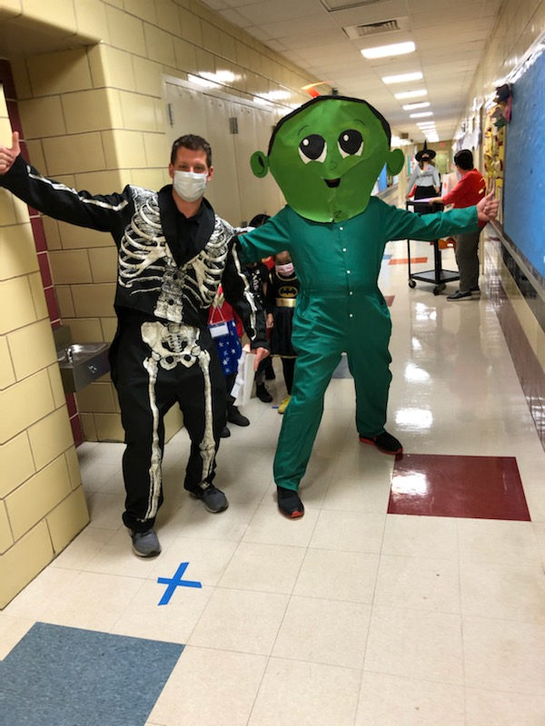 Staff member in a skeleton costume with Z the green character in the hallway