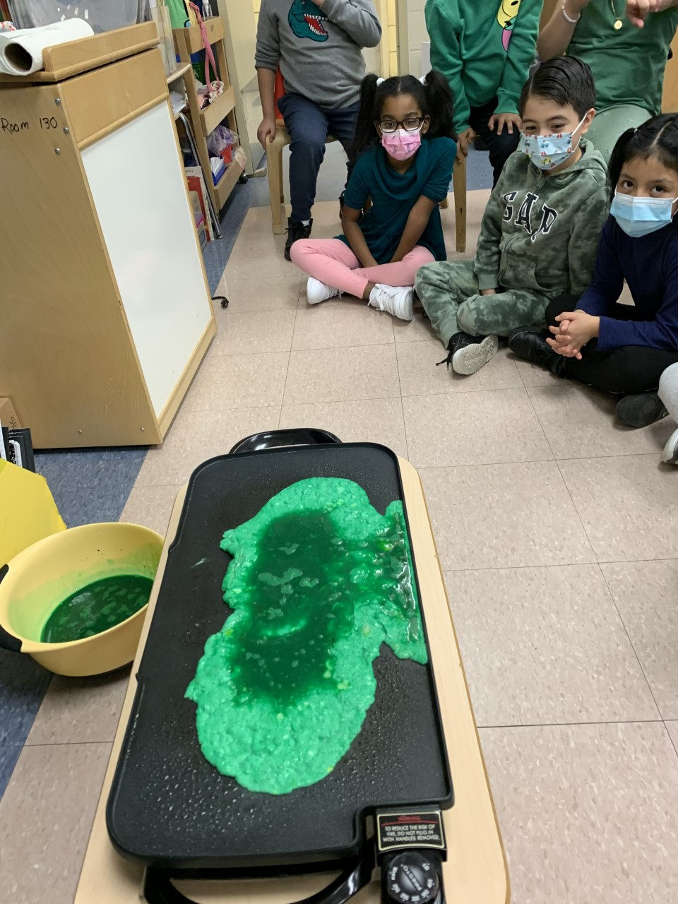 Green eggs cooking on an electric griddle as students watch