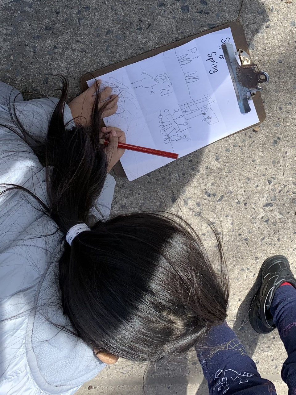 Student writing on a clipboard while sitting on the sidewalk