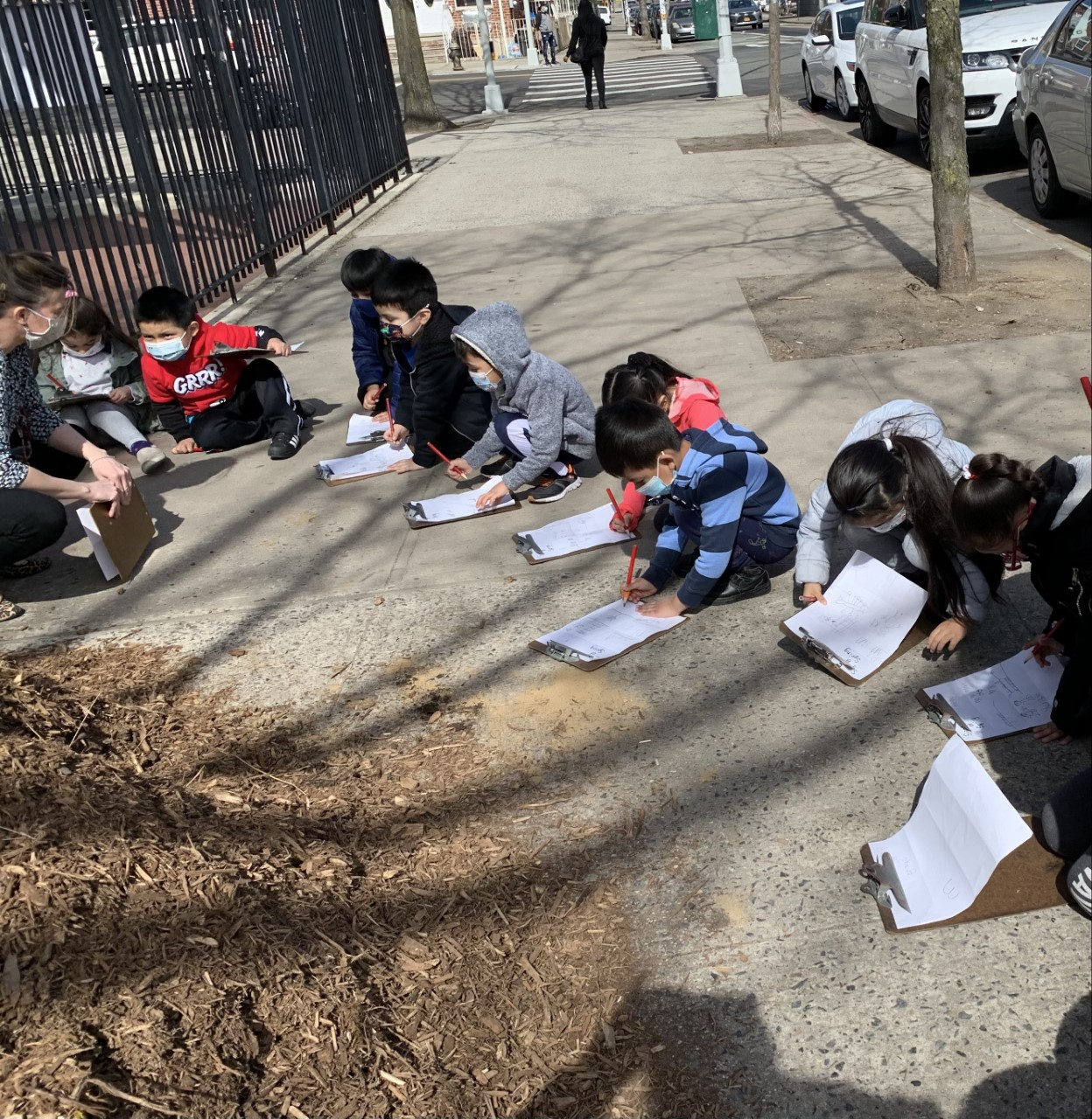 Students sitting along the sidewalk writing observations on clipboards