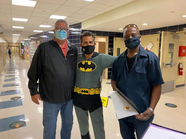 Principal in a Batman costume with two staff members in the hallway