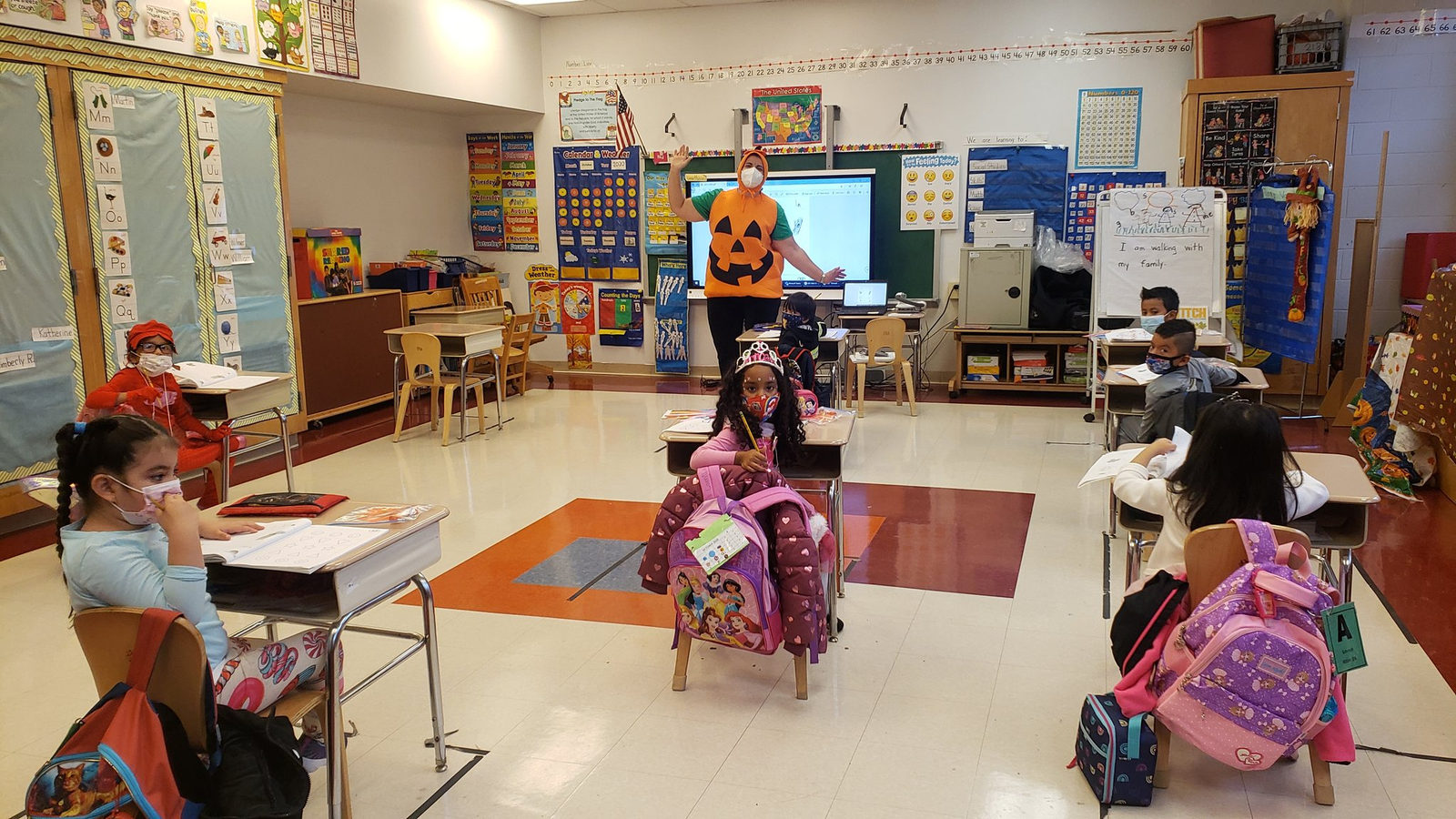 Students in Halloween costumes seated at spaced-out desks
