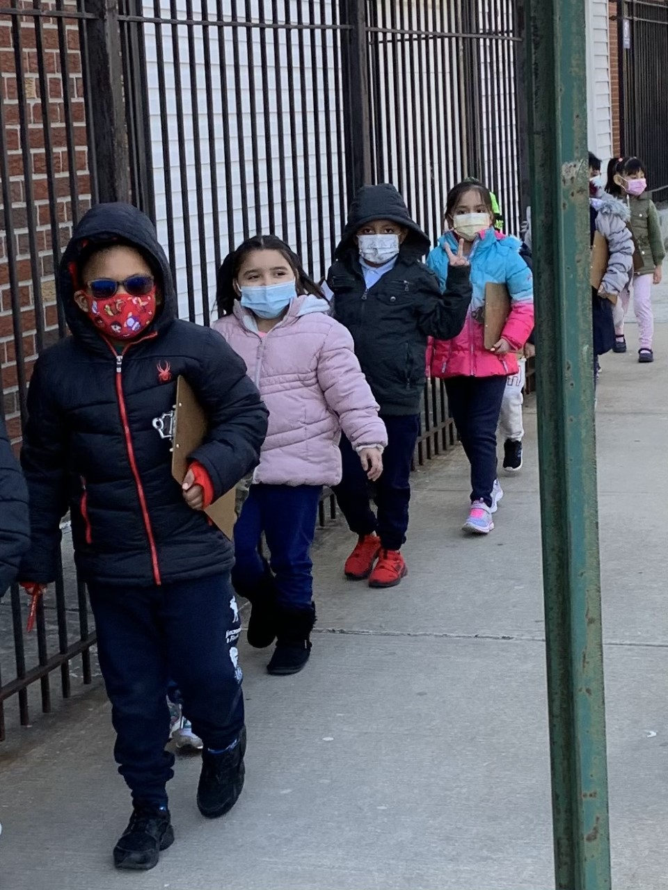 Students in masks walking in a line on the sidewalk