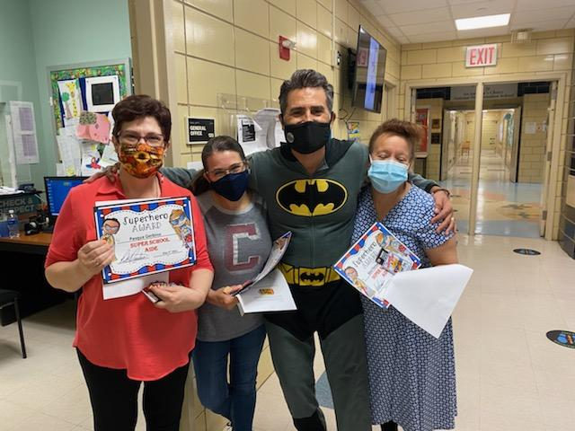 Principal in a Batman costume with staff members holding certificates