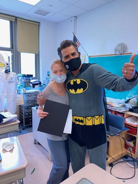 Principal in a Batman costume giving a thumbs up with a staff member