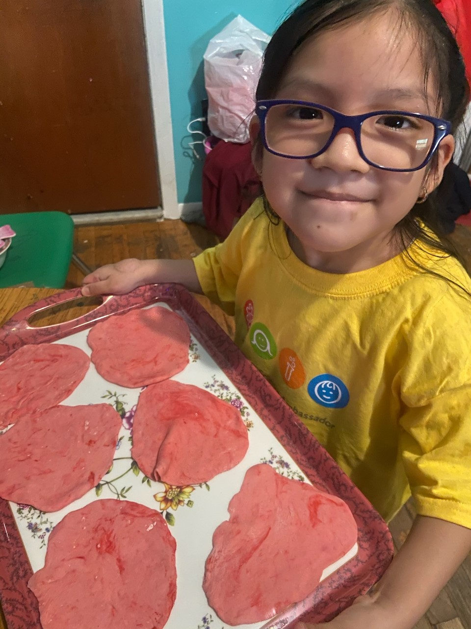 Student in glasses holding a tray of pink handprint art