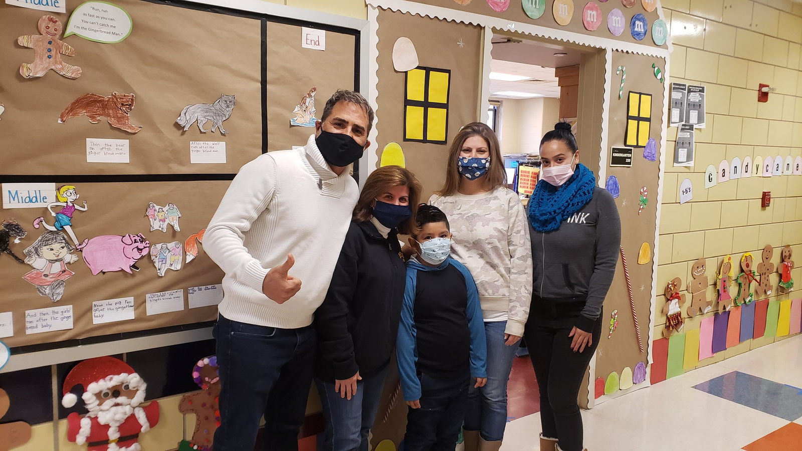 Principal, teachers and a student in front of a gingerbread hallway display