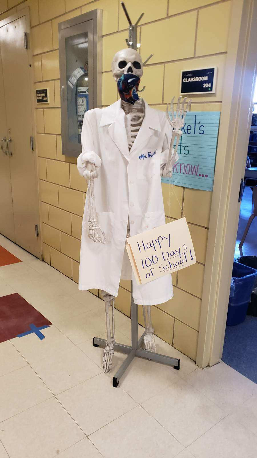 Skeleton in a lab coat with a Happy 100 Days of School sign
