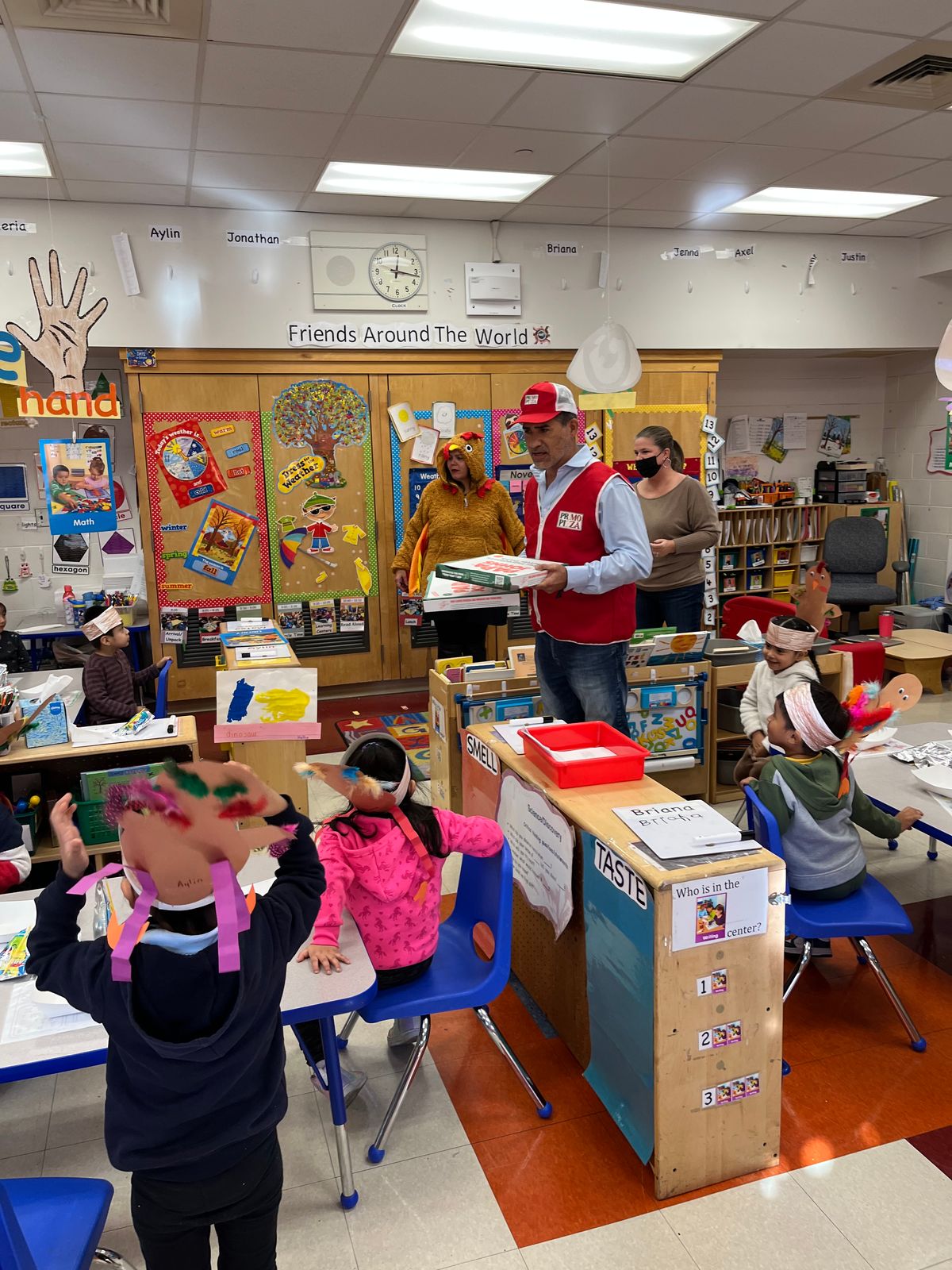 Visitors in red vests and a teacher in a turkey costume visiting a classroom