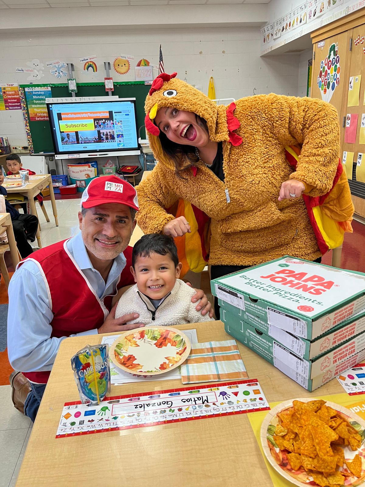 Visitor in a red vest and a teacher in a turkey costume with a student and pizza boxes