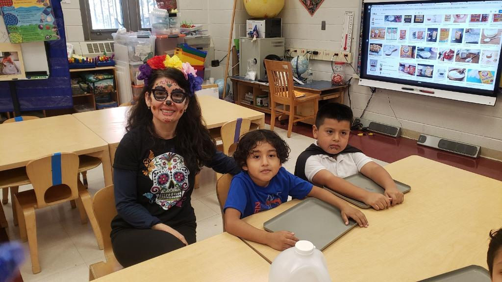 Teacher in sugar skull face paint with two students
