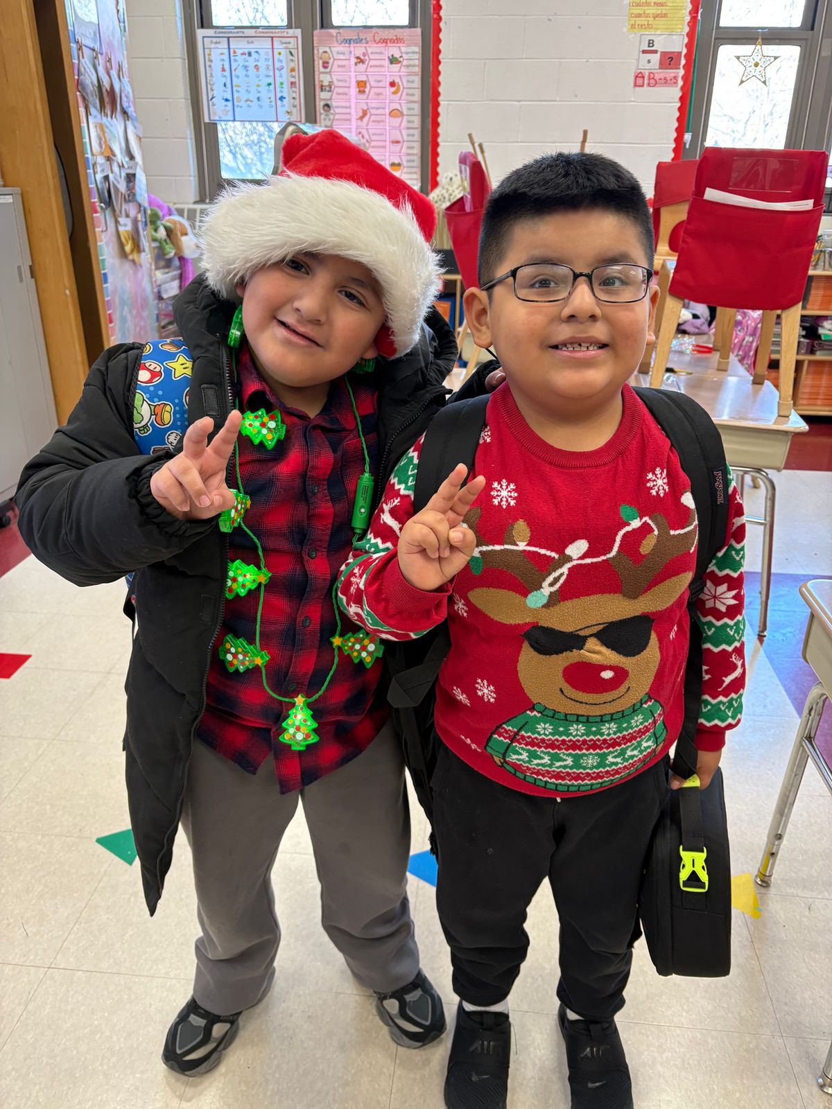 Two students in holiday sweaters and a Santa hat smiling in class