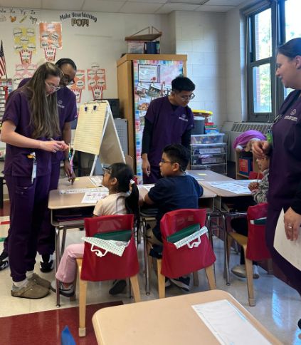 Visitors in purple scrubs working with a class