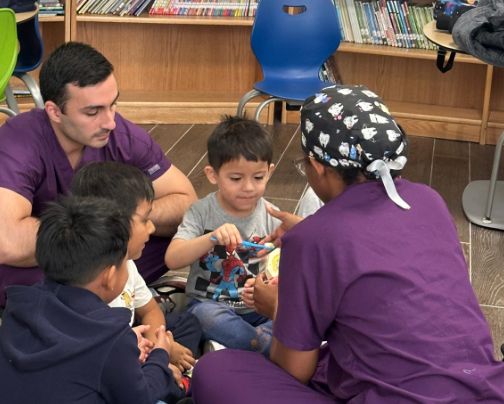 Visitor in purple scrubs showing students a tooth model up close