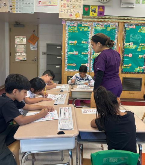 Visitor in purple scrubs checking students' work at their desks
