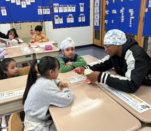 Visitor in a scrub cap showing a tooth model to students at their desks