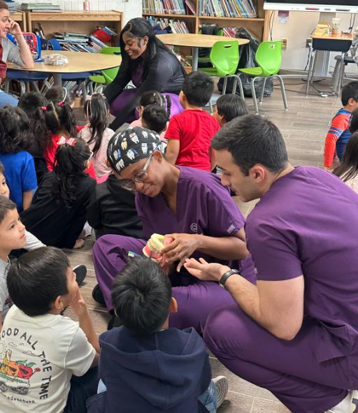 Visitors in purple scrubs showing a tooth model to students on the floor