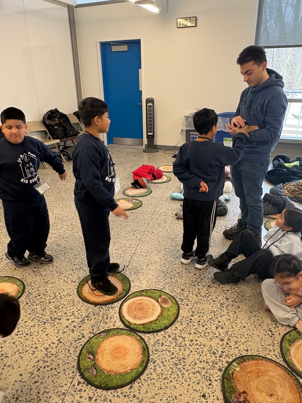 Students gathered in a classroom with tree-stump seats as a teacher leads an activity