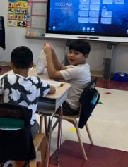 Students at their desks in front of the classroom smartboard