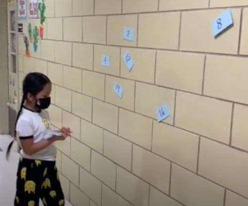 A student searching for numbered index cards taped to a wall during a scavenger hunt