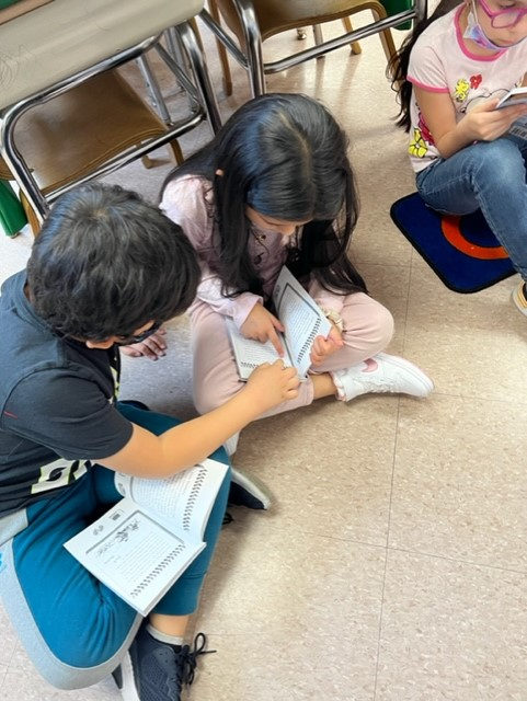 Edwin sits on the classroom floor helping a friend read