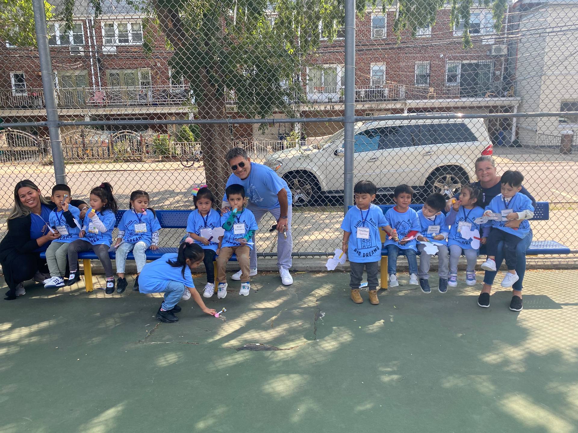 P.S. 28 students in their sky-blue P.S. 28 shirts on a bench in the schoolyard with their teachers.
