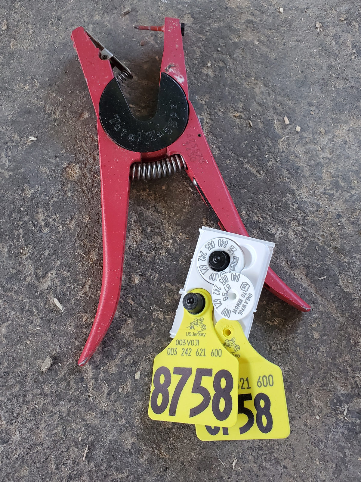 A yellow ear tag numbered 8758 and the red tagger used to attach it