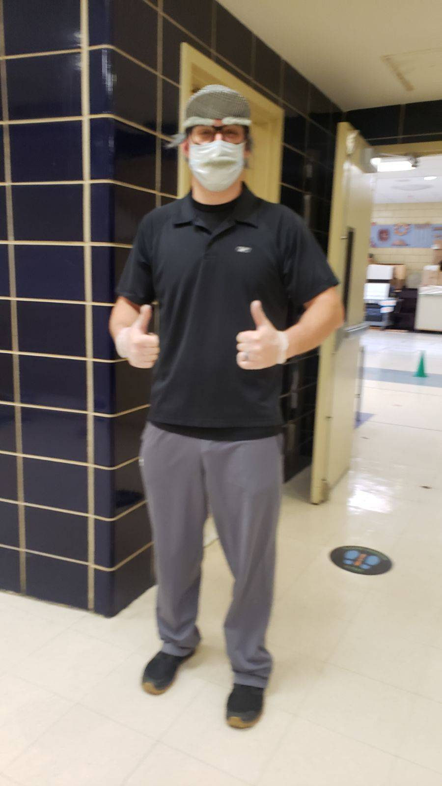 Physical education teacher giving two thumbs up in the school hallway