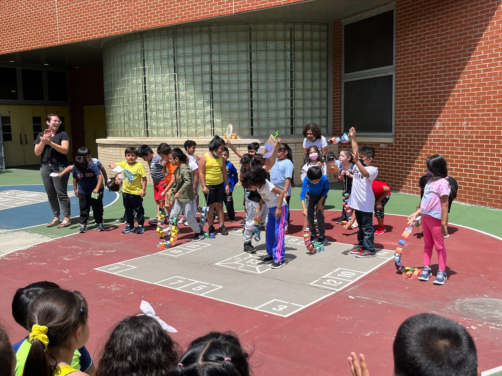 Students perform with their paper puppets in the schoolyard alongside a Puppetry in Practice teaching artist