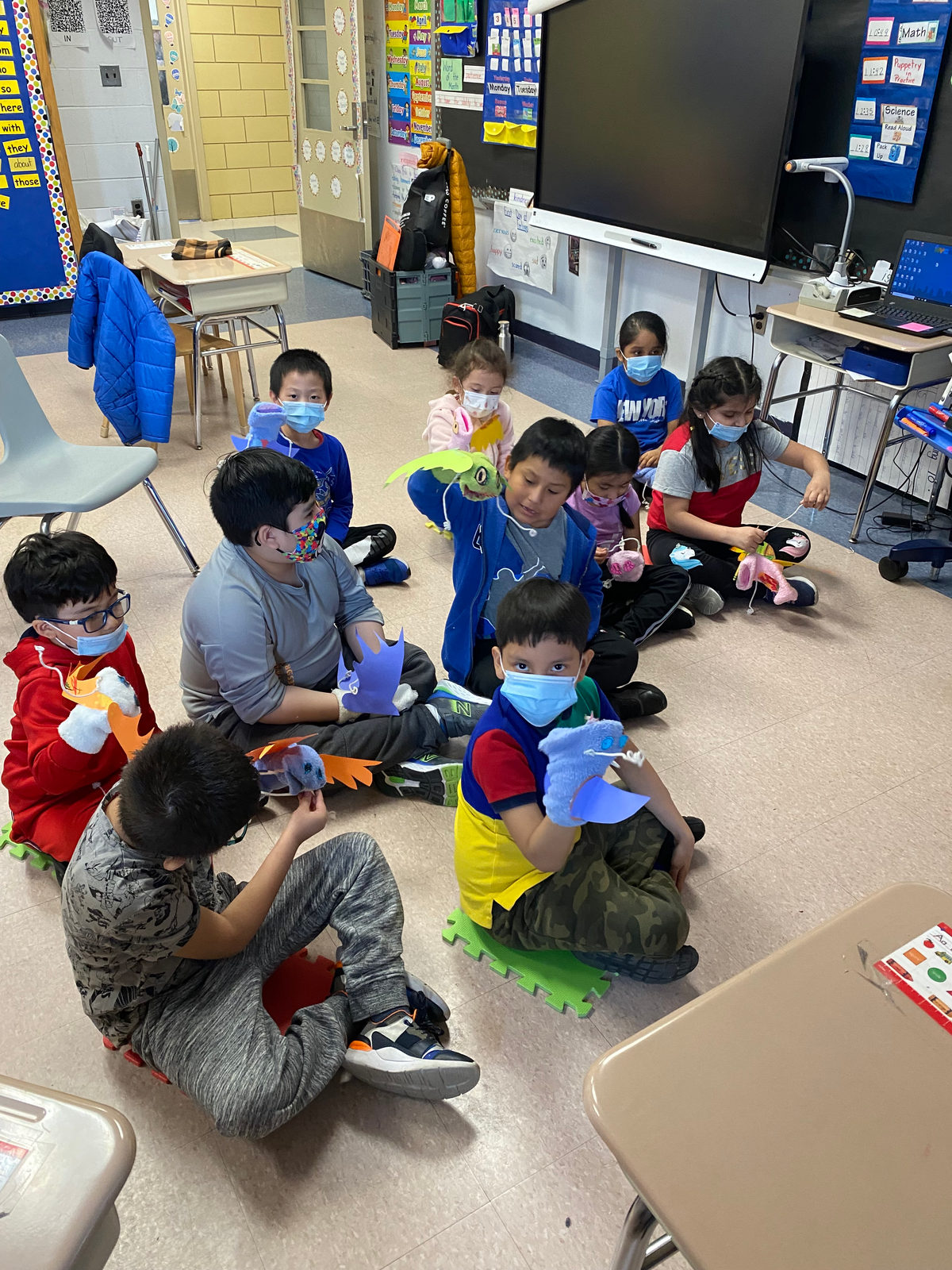 Students sit on the classroom floor wearing their hand puppets