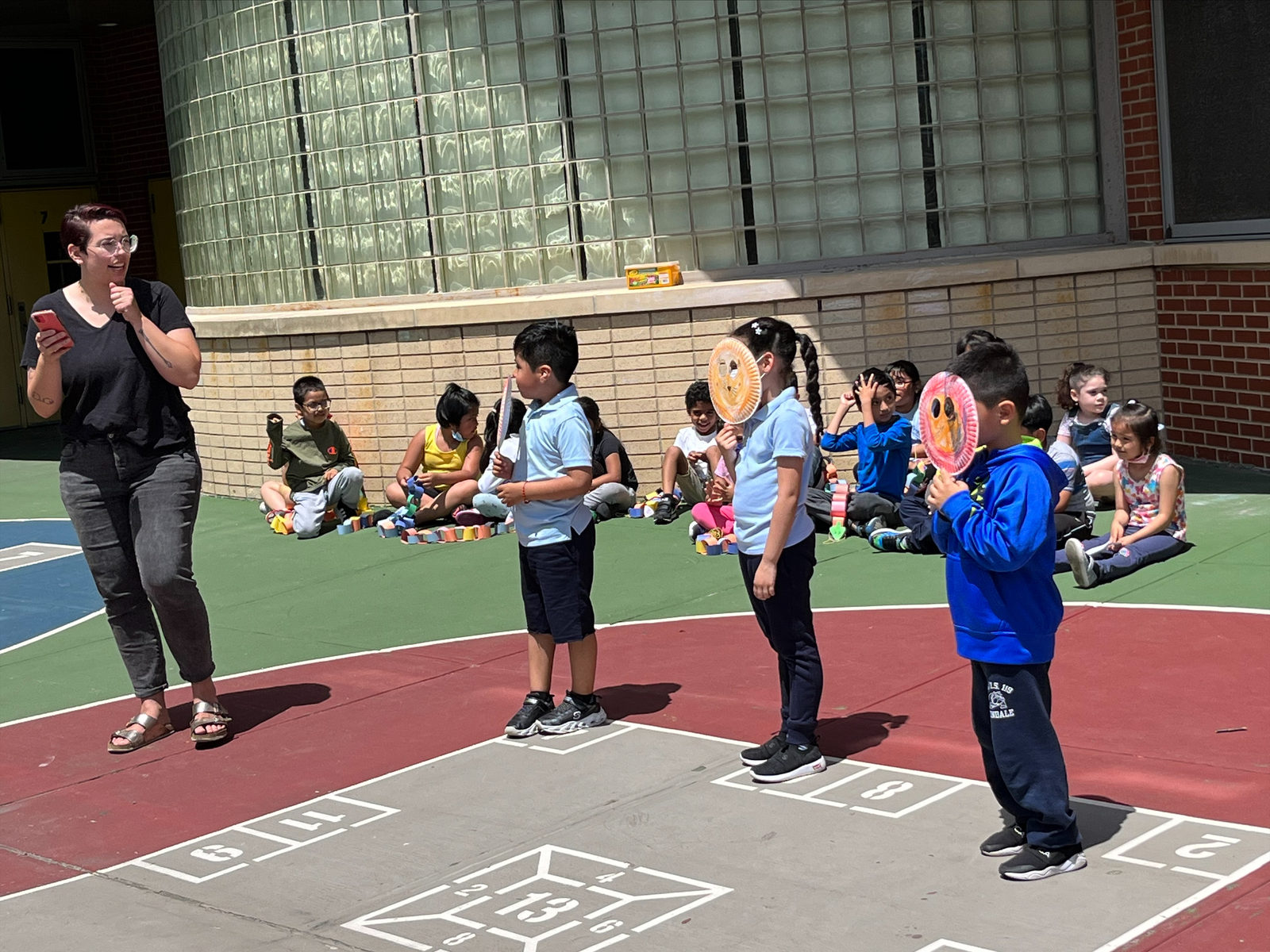Students perform with their paper puppets in the schoolyard alongside a Puppetry in Practice teaching artist