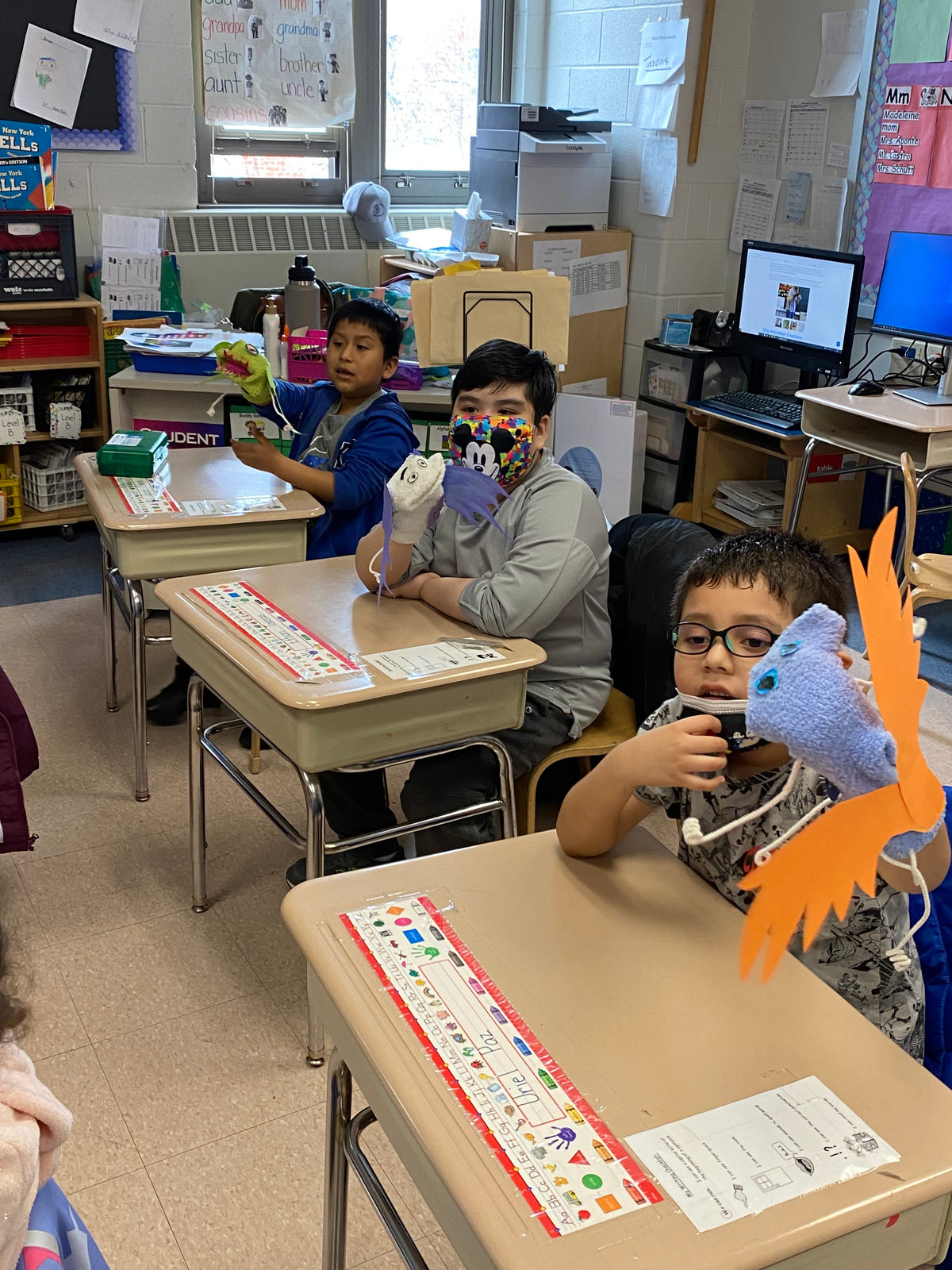 A student at his desk holds up the bird puppet he made