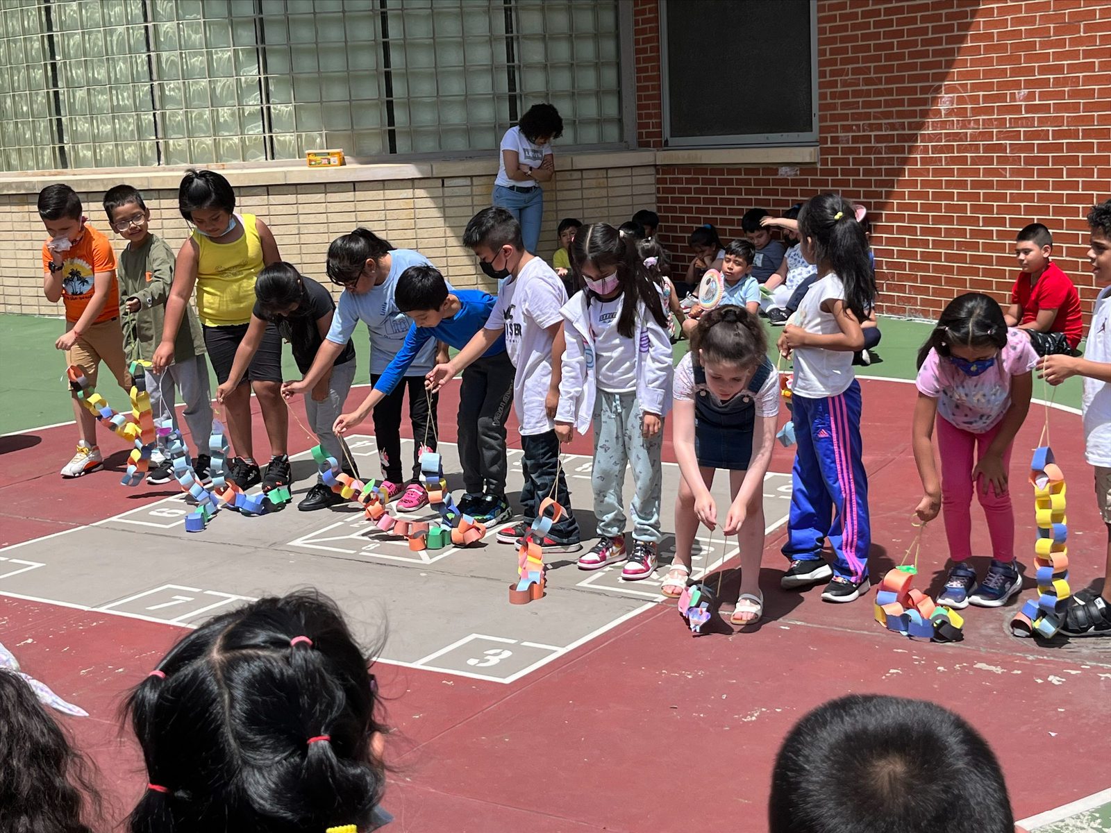 Students bend down to move their paper chain puppets along the ground