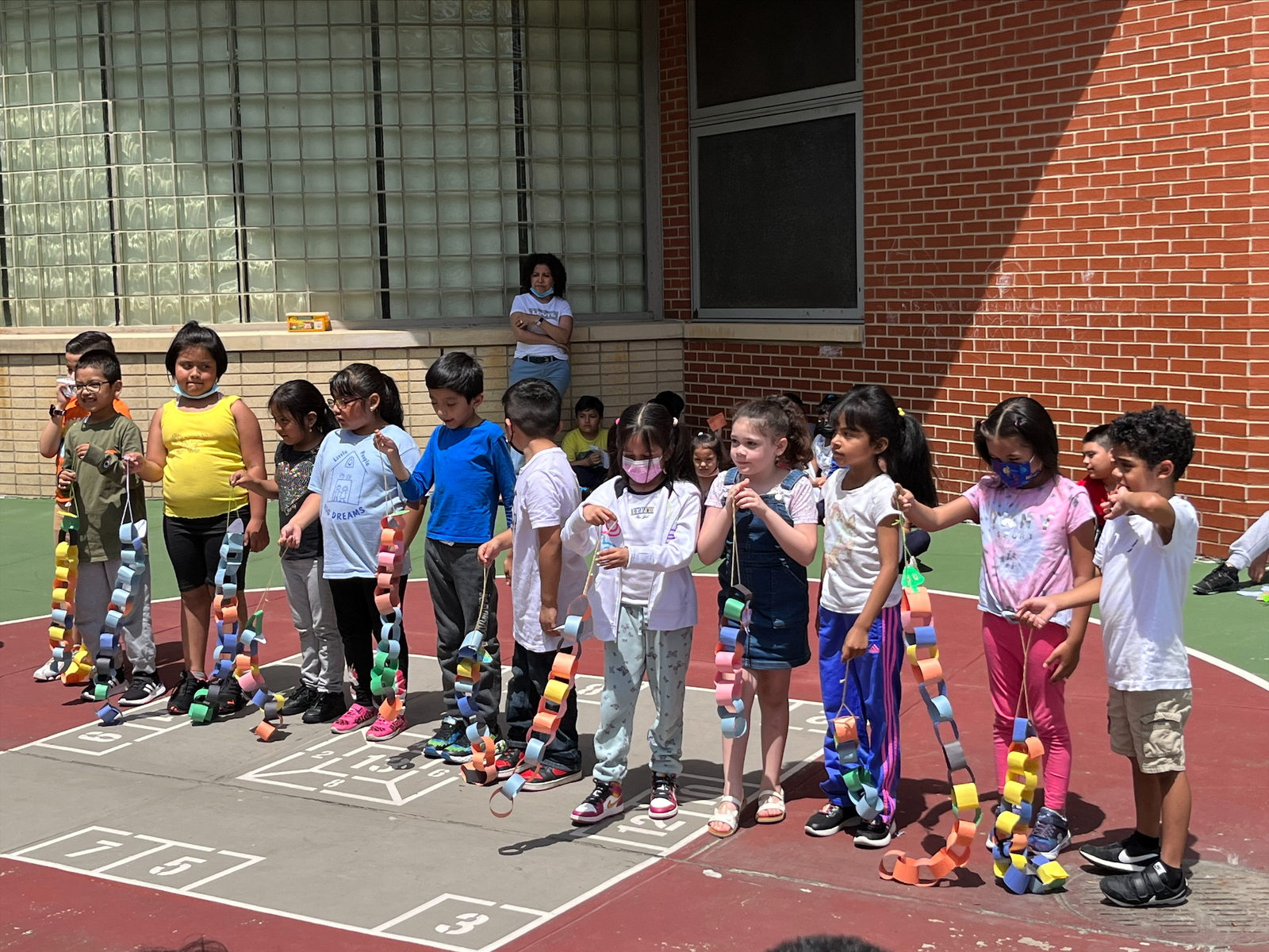 A line of students holds up long, colorful paper chain puppets in the schoolyard