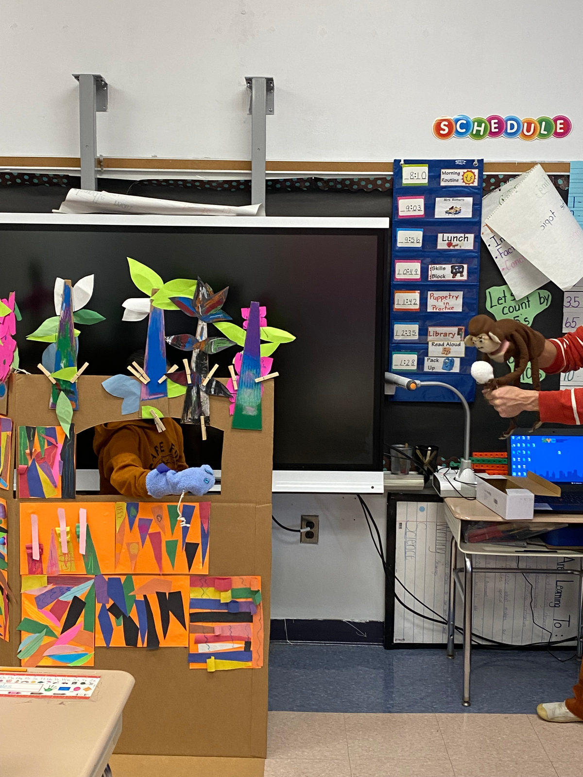 Students put on a puppet show from behind the colorful cardboard puppet stage their class built