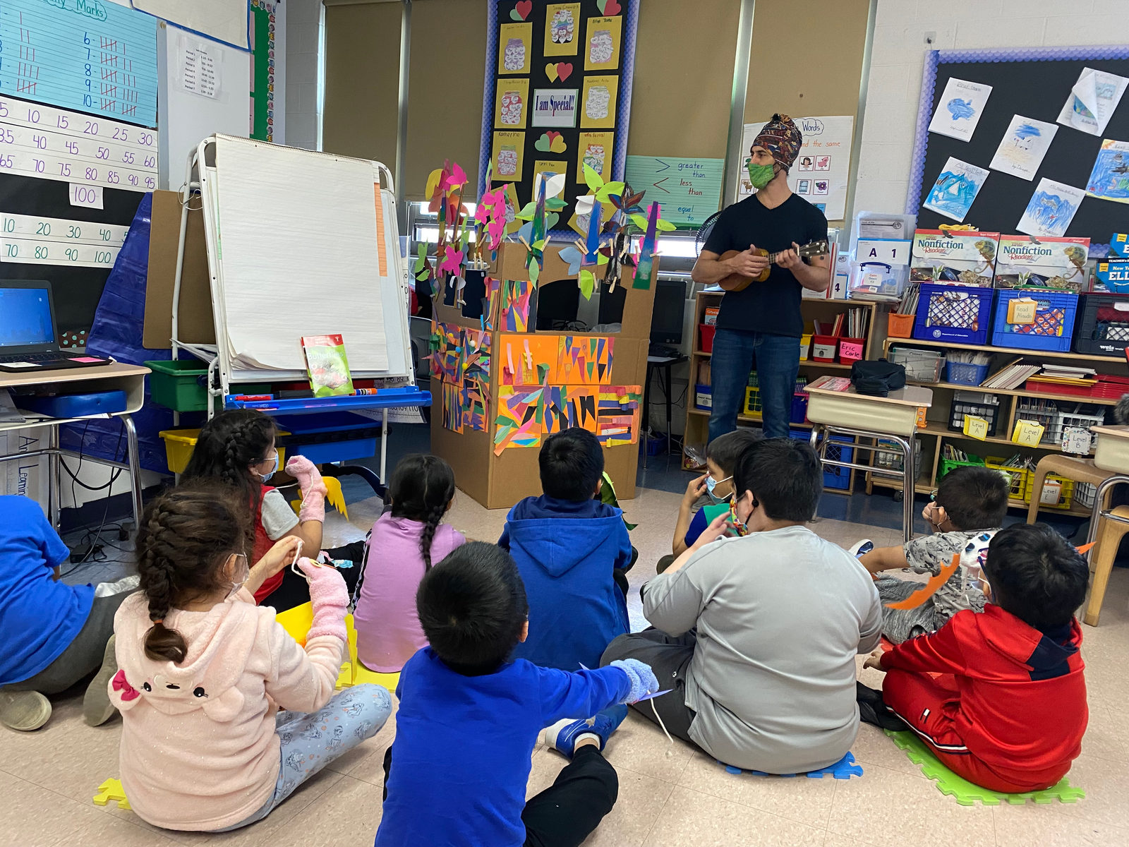 Students sit on the rug and watch a classmate's puppet show